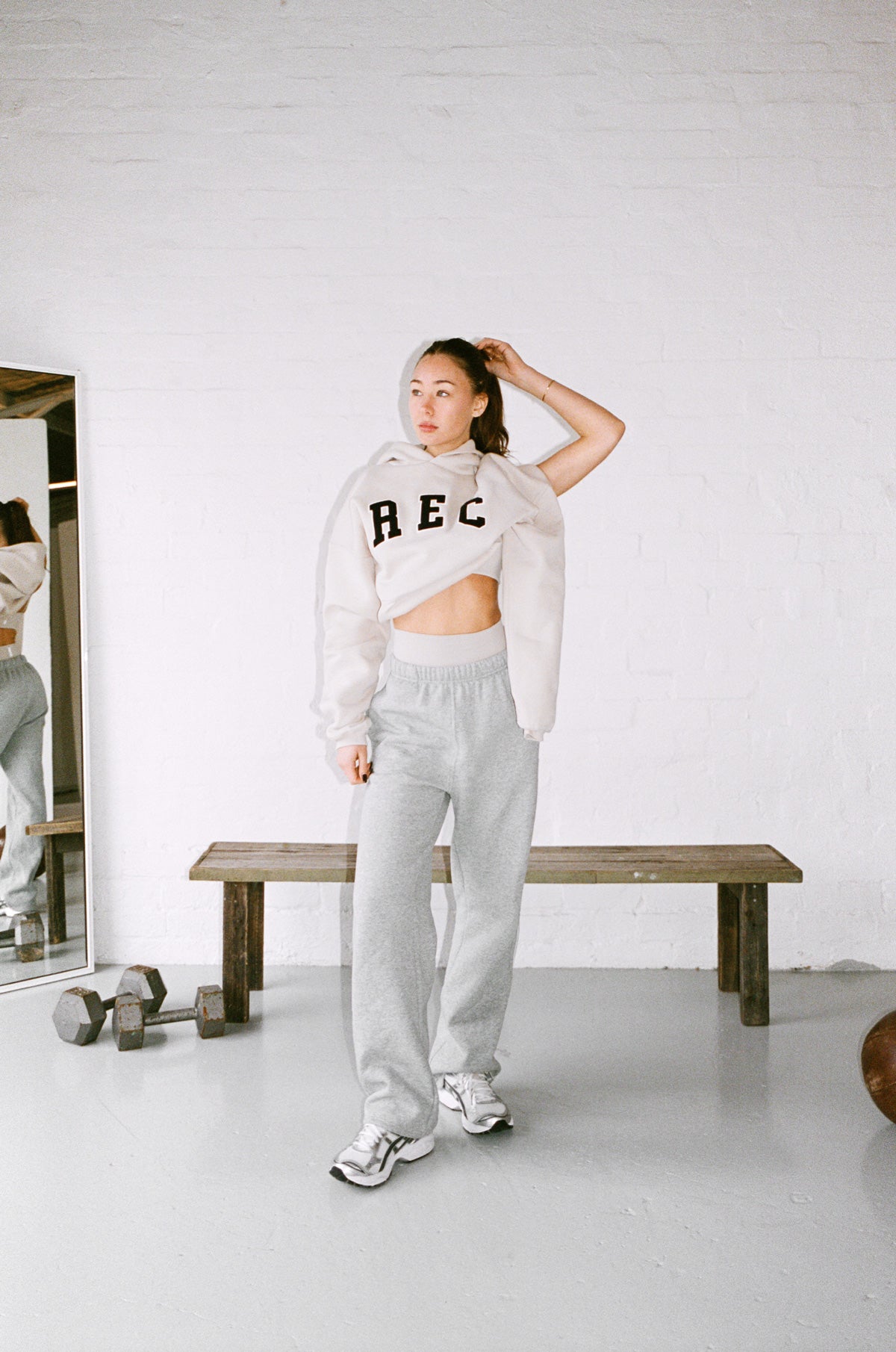 Person wearing a white oversized sweatshirt and gray sweatpants in a minimalistic room.